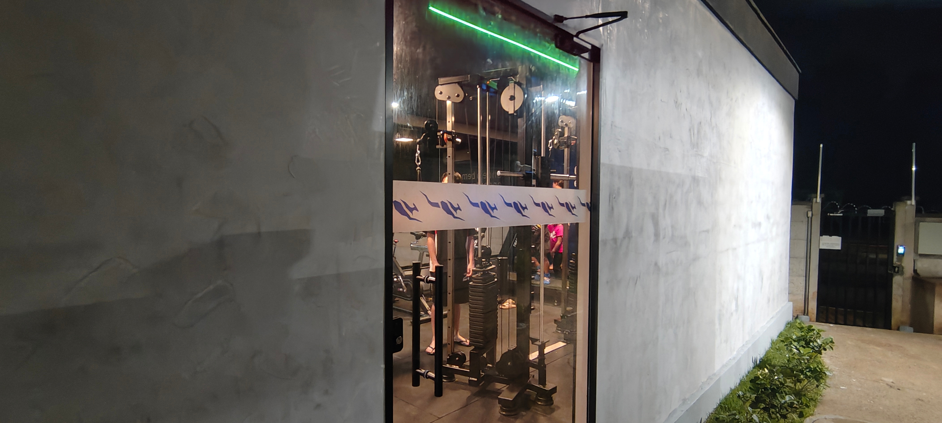 Entrada da academia condominial com equipamentos ao fundo